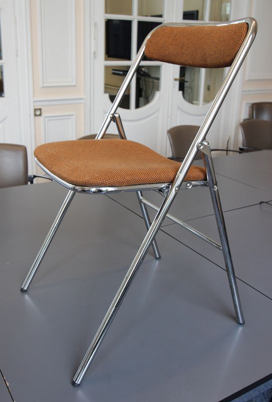 1 CHAISE PLIANTE EN METAL CHROME ET GARNITURE DE TISSU FAUVE. LOT VENDU A L'UNITE AVEC FACULTE DE REUNION.