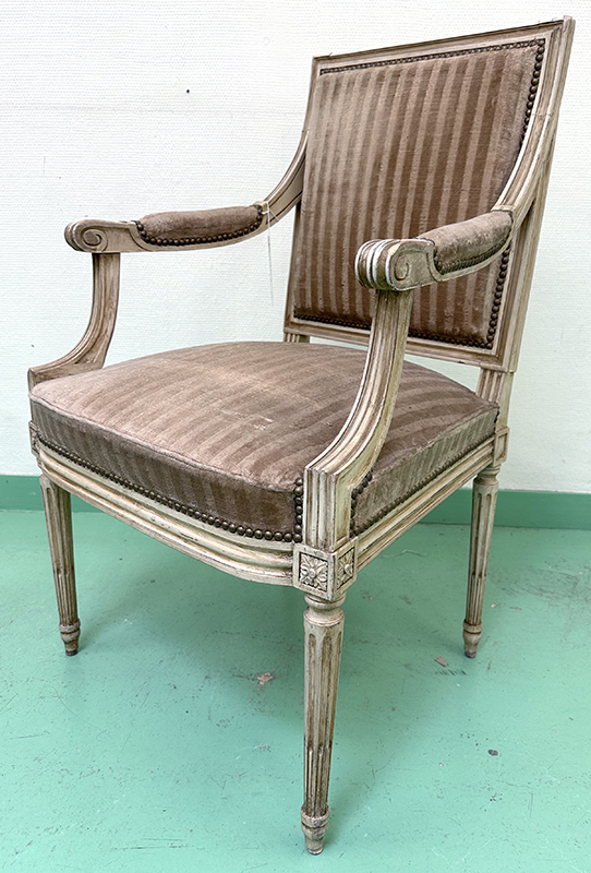 FAUTEUIL DE STYLE LOUIS XVI DOSSIER ACCOUDOIR ET ASSISE EN VELOURS CLOUTE RAYE DANS LES TONS NOISETTE ET MARRON GLACE, STRUCTURE EN BOIS SCULPTE ET PIEDS CANELES PEINTS DE COULEUR BLANC CASSE. 98 X 59 X 56 CM.  LOCALISATION : ARCUEIL RESERVE 00 SALLE 14