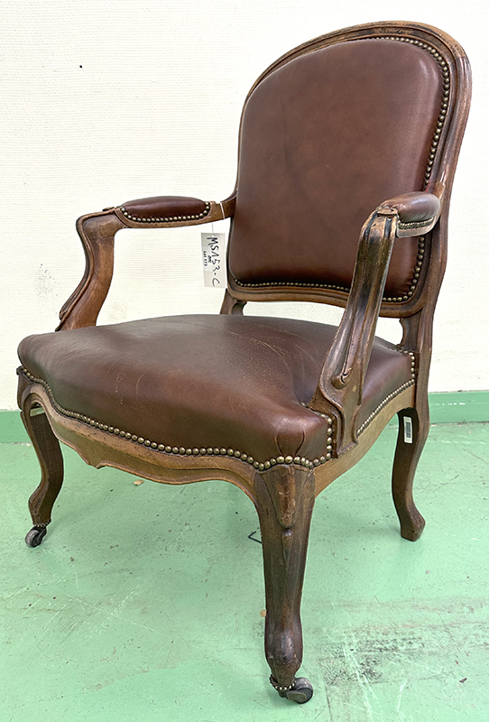 FAUTEUIL DE STYLE LOUIS XV, DOSSIER, ASSISE ET ACCOUDOIRS EN CUIR CLOUTE DE COULEUR FAUVE REPOSANT SUR UNE STRUCTURE ET 4 PIEDS EN CHENE SCULPTE AVEC ROULETTES. 85 X 68 X 63 CM. ARCUEIL 3 0014. LOCALISATION : ARCUEIL RESERVE 00 SALLE 14