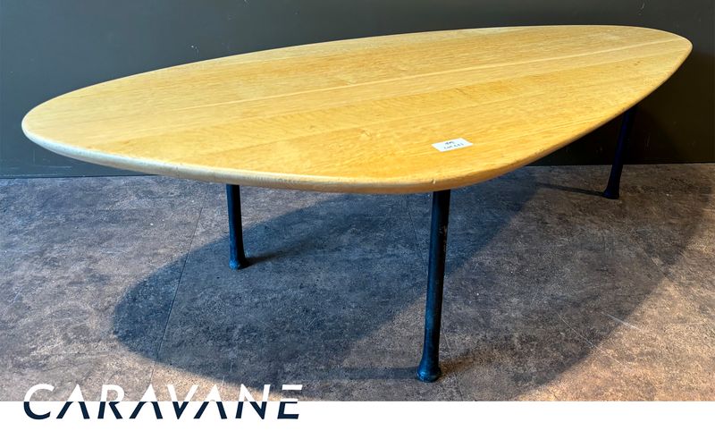 TABLE BASSE DANS LE GOUT SCANDINAVE DES ANNEES 1950 DE MARQUE CARAVANE MODELE YOMI, PLATEAU DE FORME OVOIDE EN CHENE NATUREL REPOSANT SUR 3 PIEDS EN FER FORGE. 41 X 136 X 64 CM.