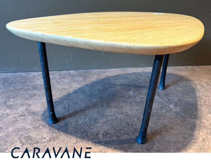 TABLE BASSE DANS LE GOUT SCANDINAVE DES ANNEES 1950 DE MARQUE CARAVANE MODELE YOMI, PLATEAU DE FORME OVOIDE EN CHENE NATUREL REPOSANT SUR 3 PIEDS EN FER FORGE. 41 X 81 X 57 CM.