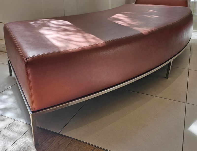 BANQUETTE HARICOT ASSISE EN CUIR DE COULEUR TERRACOTTA REPOSANT SUR UNE STRUCTURE EN ACIER CHROME. 43 X 223 X 90 CM. LOCALISATION -> BAT A : ACCUEIL