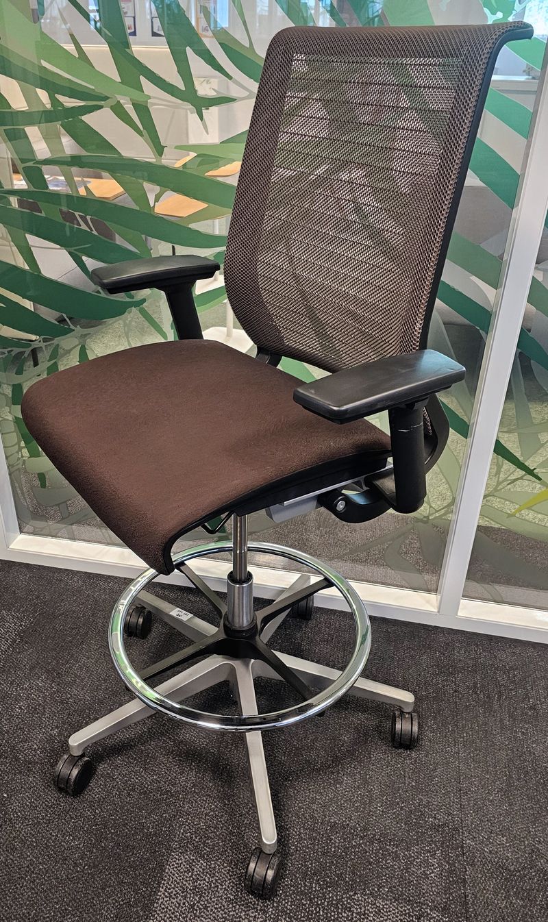 FAUTEUIL DE BUREAU HAUT A HAUTEUR DOSSIER ET ACCOUDOIRS AJUSTABLES DE MARQUE STEELCASE MODELE THINK, DOSSIER EN RESILLE DE COULEUR MARRON ET ASSISE EN TISSU DE COULEUR MARRON REPOSANT SUR UN PIETEMENT AVEC REPOSE PIED EN ACIER CHROME. HAUTEUR MAX : 125 CM ; HAUTEUR MIN : 105 CM ; 70 X 70 CM. LOCALISATION -> BAT A : RDC E