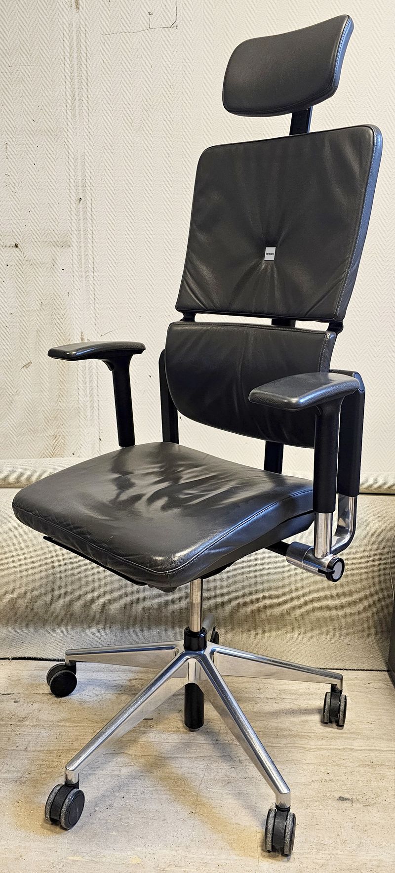 FAUTEUIL ERGONOMIQUE SUR ROULETTE A HAUTEUR ET TETIERE AJUSTABLE, ASSISE, DOSSIER, TETIERE ET ACCOUDOIRS EN CUIR DE COULEUR NOIR REPOSANT SUR UN PIETEMENT ETOILE A 5 BRANCHE EN ACIER CHROME DE MARQUE STEELCASE MODELE PLEASE. HAUTEUR MAX : 140 CM, HAUTEUR MIN : 128 CM, 70 X 63 CM. LOCALISATION -> BAT B : STOCK DELTA