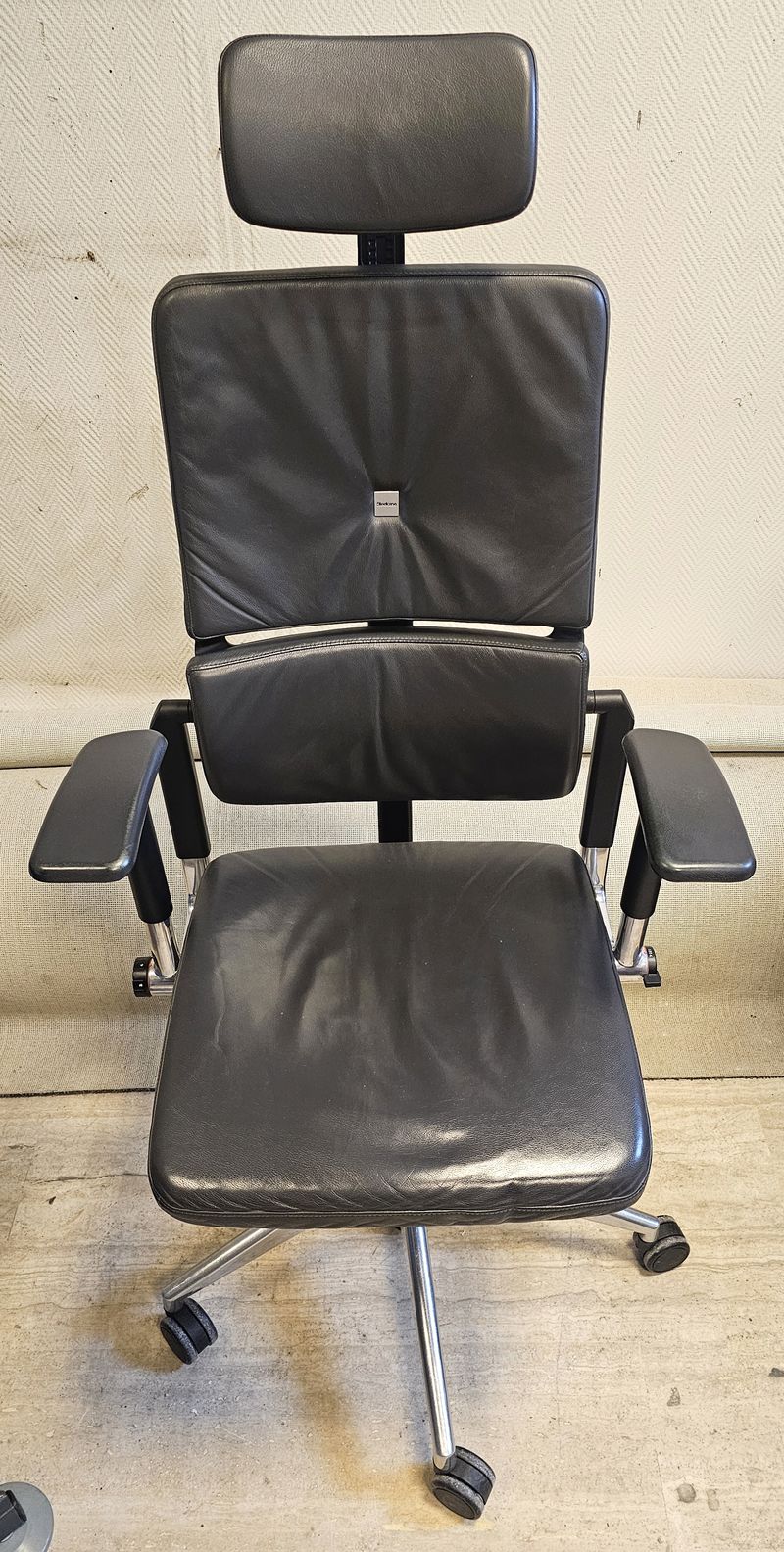 FAUTEUIL DE DIRECTION SUR ROULETTE A HAUTEUR ET TETIERE AJUSTABLE, ASSISE, DOSSIER, TETIERE ET ACCOUDOIRS EN CUIR DE COULEUR NOIR REPOSANT SUR UN PIETEMENT ETOILE A 5 BRANCHE EN ACIER CHROME DE MARQUE STEELCASE MODELE PLEASE. HAUTEUR MAX : 140 CM, HAUTEUR MIN : 128 CM, 70 X 63 CM. LOCALISATION -> BAT B : STOCK DELTA