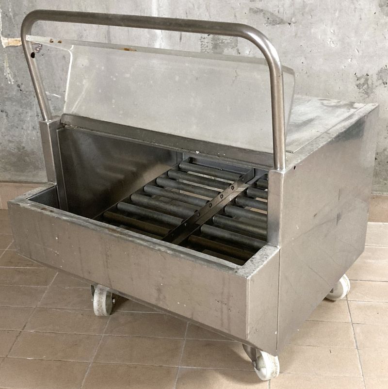 CHARIOT A ROULEAUX EN INOX ALIMENTAIRE OUVRANT EN FACADE PAR UNE TRAPPE EN INOX ALIMENTAIRE ET PAR DERRIERE PAR UNE TRAPPE EN PLASTIQUE TRANSPARENT SUR UN ESPACE AVEC 2 RANGEES DE 9 ROULEAUX EN INOX ET REPOSANT SUR 4 ROULETTES DIRECTIONNELLES EN NYLON BLANC. 75 X 61 X 62 CM.