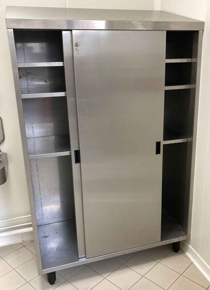 ARMOIRE A CHAPEAU INCLINE EN INOX ALIMENTAIRE OUVRANT PAR 2 PORTES COULISSANTES SUR 3 ETAGERES ET REPOSANT SUR 4 PIEDS. AVEC CLES. 193 X 120 X 61 CM.