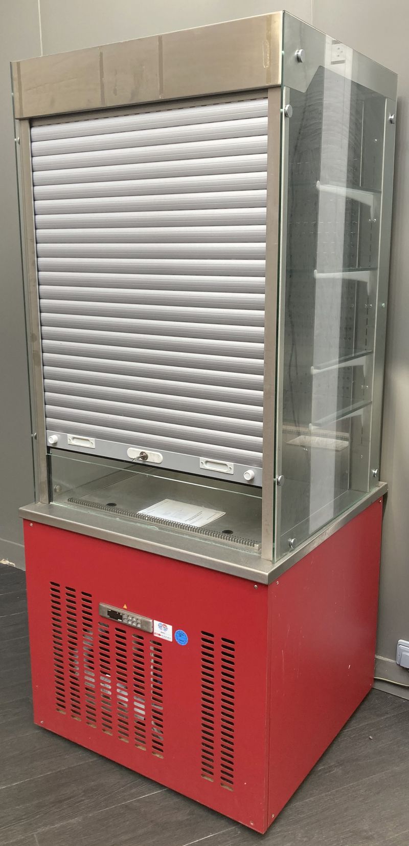 VITRINE DE SERVICE REFRIGEREE POSITIVE DE MARQUE VAUCONSTANT EN INOX ALIMENTAIRE, VERRE ET BOIS LAQUE ROUGE OUVRANT PAR UN RIDEAU EN PLASTIQUE GRIS SUR 4 ETAGERES EN VERRE. GROUPE FROID INTEGRE. AVEC CLE. 193 X 82 X 80 CM.