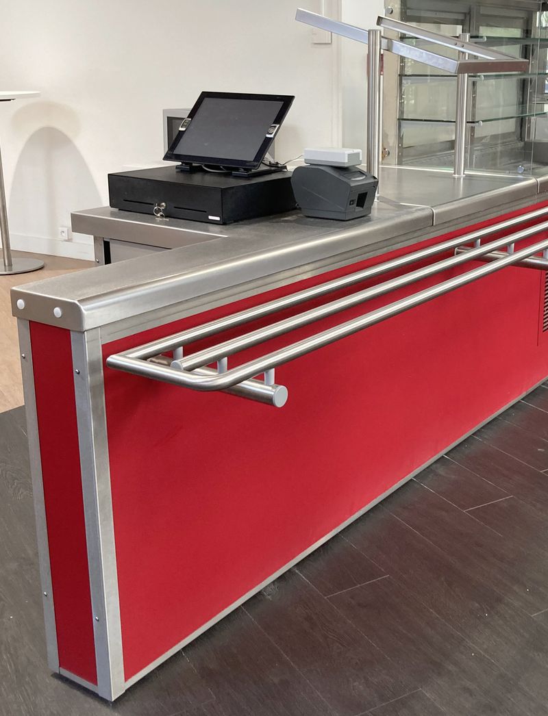 ILOT DE CAISSE ET SUPPORT A PANIER DE MARQUE VAUCONSTANT EN INOX ALIMENTAIRE, VERRE ET BOIS LAQUE ROUGE, AVEC 3 PRISES 230V REPOSANT SUR 4 PIEDS. 135 X 193 X 83 CM.