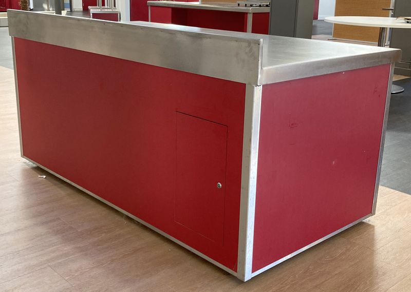 BUFFET ADOSSE DE MARQUE VAUCONSTANT EN INOX ALIMENTAIRE, VERRE ET BOIS LAQUE ROUGE PLATEAU EN INOX, AVEC TRAPPE DE SERVICE COMPRENANT 4 PRISES 230V. 96,5 X 200 X 100 CM.