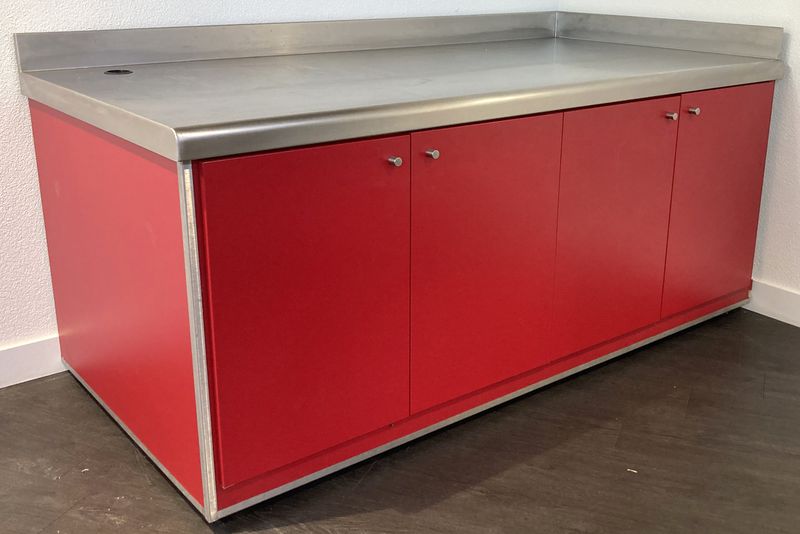 BUFFET ADOSSE DE MARQUE VAUCONSTANT EN INOX ALIMENTAIRE, VERRE ET BOIS LAQUE ROUGE PLATEAU EN INOX AVEC 1 TROU, OUVRANT EN FACADE PAR 4 PORTES SUR 8 NICHES, AVEC TRAPPE DE SERVICE. 96,5 X 200 X 100 CM.