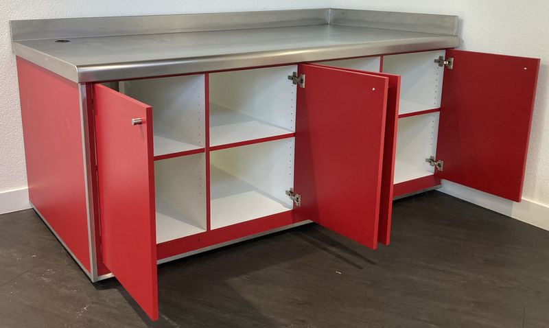 BUFFET ADOSSE DE MARQUE VAUCONSTANT EN INOX ALIMENTAIRE, VERRE ET BOIS LAQUE ROUGE PLATEAU EN INOX AVEC 1 TROU, OUVRANT EN FACADE PAR 4 PORTES SUR 8 NICHES, AVEC TRAPPE DE SERVICE. 96,5 X 200 X 100 CM.