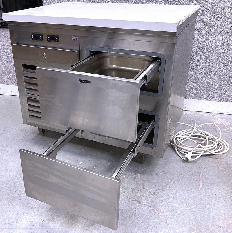 MEUBLE BAS REFRIGERE EN INOX SURMONTE D'UNE PLANCHE DE DECOUPE EN NYLON ALIMENTAIRE OUVRANT PAR 2 TIROIRS A BACS GASTRO EN FACADE AVEC GROUPE FROID INTEGRE REPOSANT SUR 4 PIEDS. 89 X 100 X 70 CM