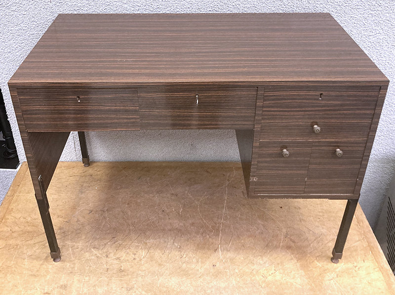 BUREAU EN FORMICA SOMBRE OUVRANT PAR 6 TIROIRS EN FACADE DONT 3 FERMANT A CLE REPOSANT SUR UNE STRUCTURE EN ACIER LAQUE NOIR A 4 PIEDS AVEC PATINS EN LAITON. AVEC SA CLEF. 77 X 110 X 60 CM.