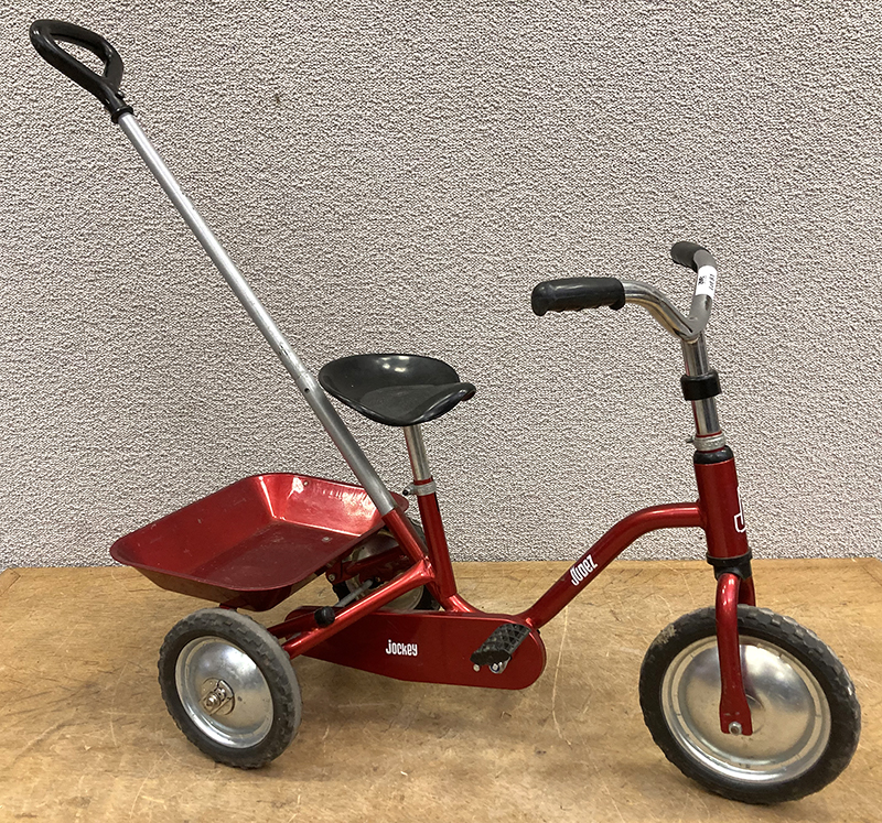 TRICYCLE A PEDALE DE MARQUE JUDEZ JOCKEY EN ACIER LAQUE ROUGE METALLISE AVEC BENNE BASCULANTE ET PERCHE D'ASSISTANCE A LA CONDUITE. 90 X 94 X 43 CM.