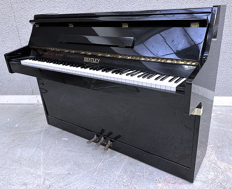 PIANO DROIT CADRE EN ACIER HABILLAGE EN BOIS LAQUE DE COULEUR NOIR DE MARQUE BENTLEY FABRIQUE EN ANGLETERRE CIRCA 1970. VENDU AVEC PROTEGE CLAVIER EN TISSUS. LOQUET DE VERROUILLAGE DE LA TRAPPE INFERIEURE HS. 98.5 X 139 X 54 CM.