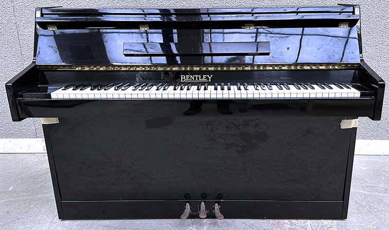 PIANO DROIT CADRE EN ACIER HABILLAGE EN BOIS LAQUE DE COULEUR NOIR DE MARQUE BENTLEY FABRIQUE EN ANGLETERRE CIRCA 1970. VENDU AVEC PROTEGE CLAVIER EN TISSUS. LOQUET DE VERROUILLAGE DE LA TRAPPE INFERIEURE HS. 98.5 X 139 X 54 CM.